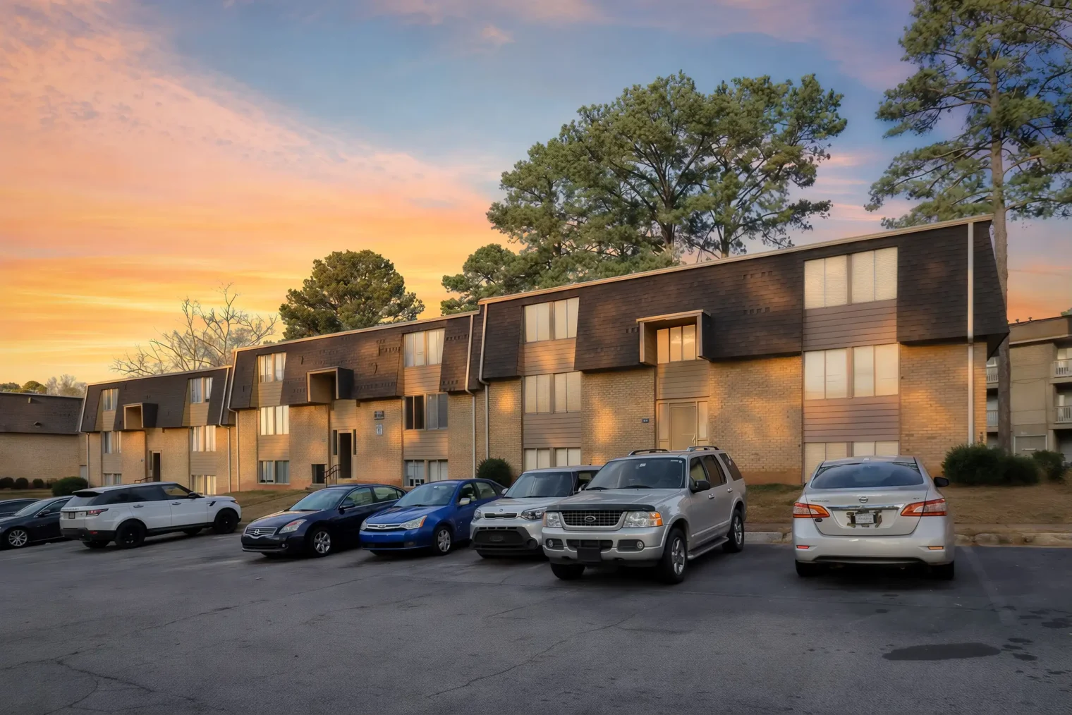 Exterior view of The Village on Riverwalk apartment buildings in College Park, GA, captured at sunset with warm evening light.